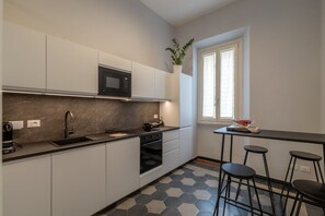 A modern kitchen with a microwave, oven, sink, and bar stools. - Toscana 8 - FromHometoRome (Roma)