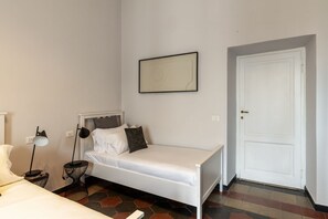 A single bed with a white mattress, a bedside table with a lamp, a framed picture on the wall, and a white door. - Toscana 8 - FromHometoRome (Roma)