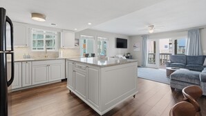 Una cocina moderna con armarios blancos, una isla grande y una zona de comedor con un sofá gris.