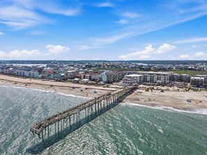 A coastal area with a pier extending into the water, beachfront buildings, and a distant cityscape. - Condo w Ocean & Pier Views! Steps to Beach, Pool, Tiki Bar & Freeman Park (Carolina Beach)