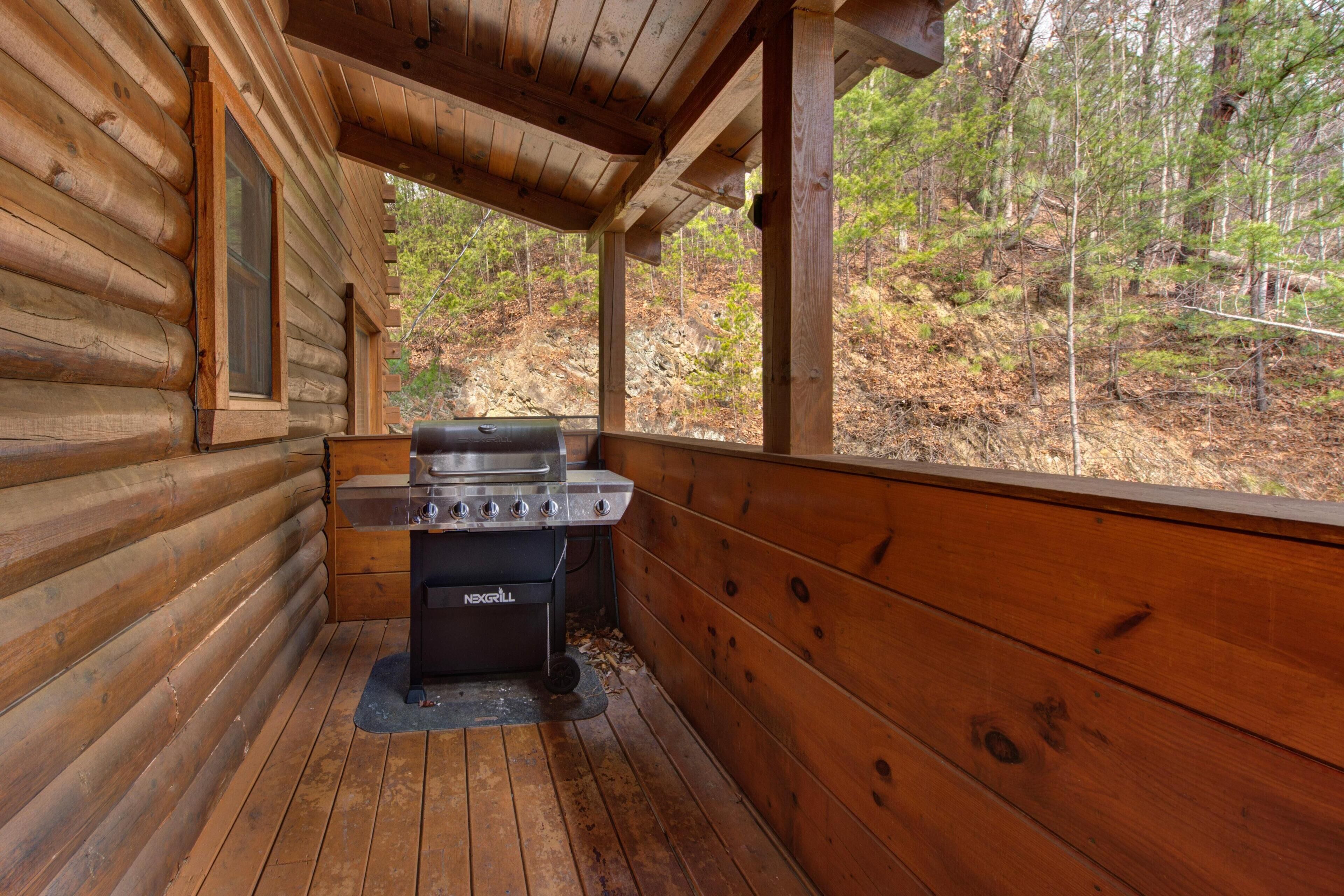 A wooden cabin with a grill area and a window overlooking a forest.