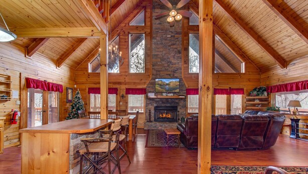 A spacious log cabin interior with a stone fireplace, wooden ceiling beams, a dining area, and a cozy seating area. - Secluded Hideaway (Pigeon Forge)