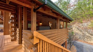 A log cabin with a wooden deck, a covered porch, and a stone wall in the background. - Secluded Hideaway (Pigeon Forge)
