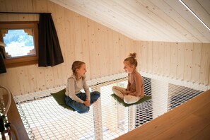 Two individuals seated on a netted platform in a room with wooden walls and a sloped ceiling.