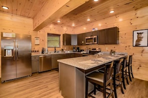 A modern kitchen with wooden walls, stainless steel appliances, a granite countertop, and bar seating. - Peaks for Itself (Sevierville)