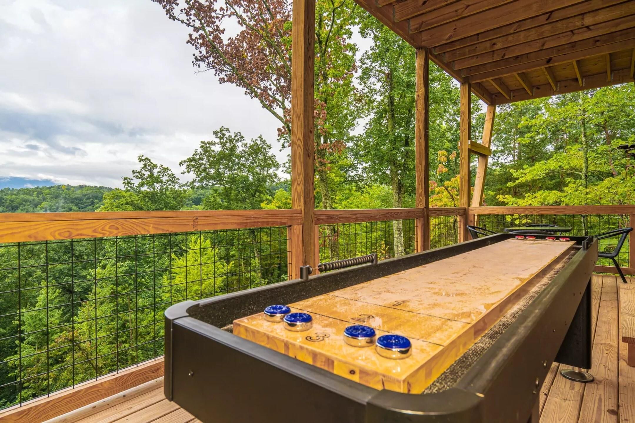 A shuffleboard table on a wooden deck with a view of a forest.