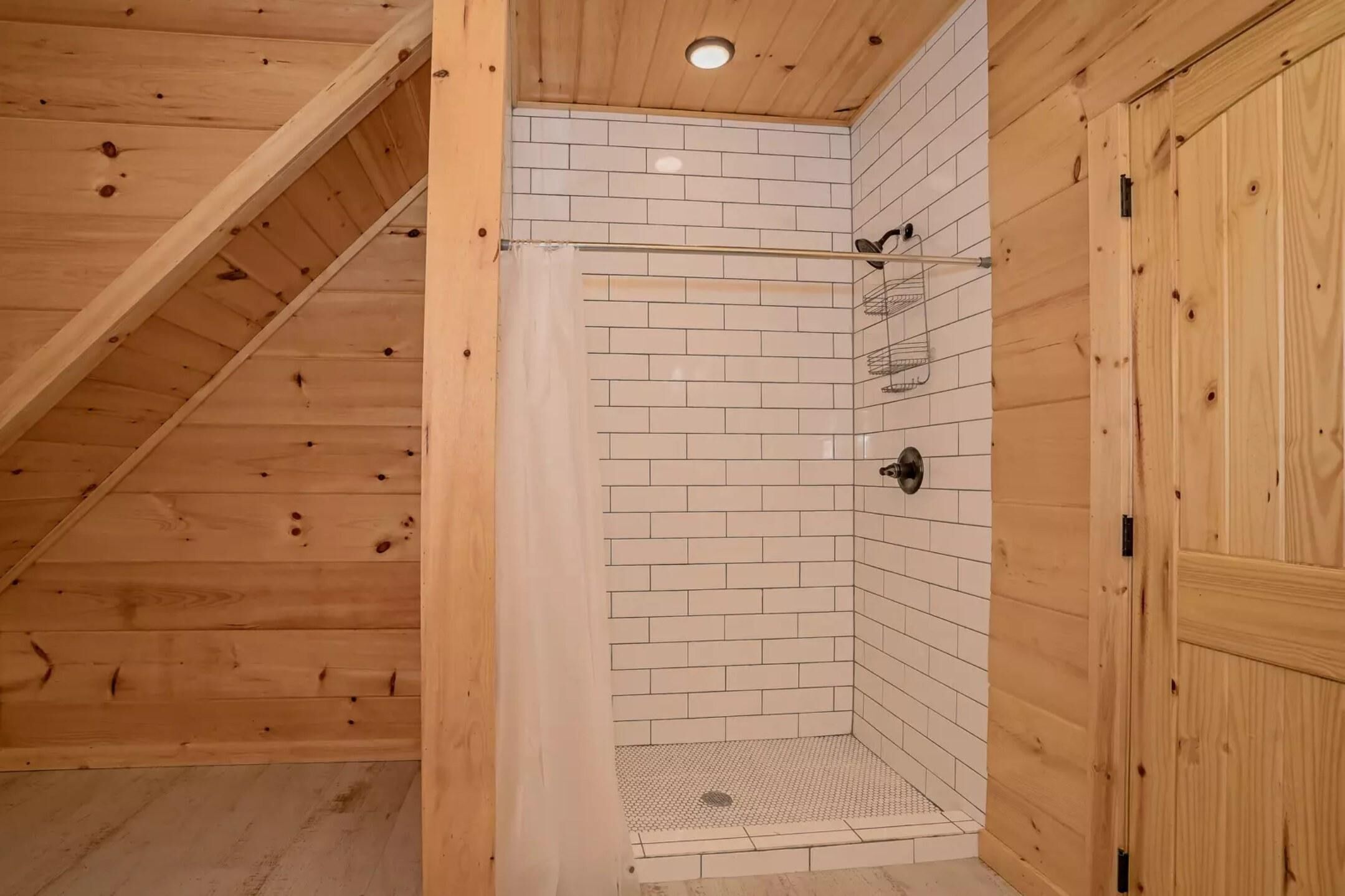 A wooden-paneled room with a tiled shower area, a wooden door, and a ceiling light.