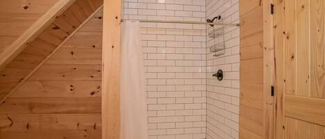 Habitación con paneles de madera, zona de ducha con azulejos, puerta de madera y una luz en el techo.
