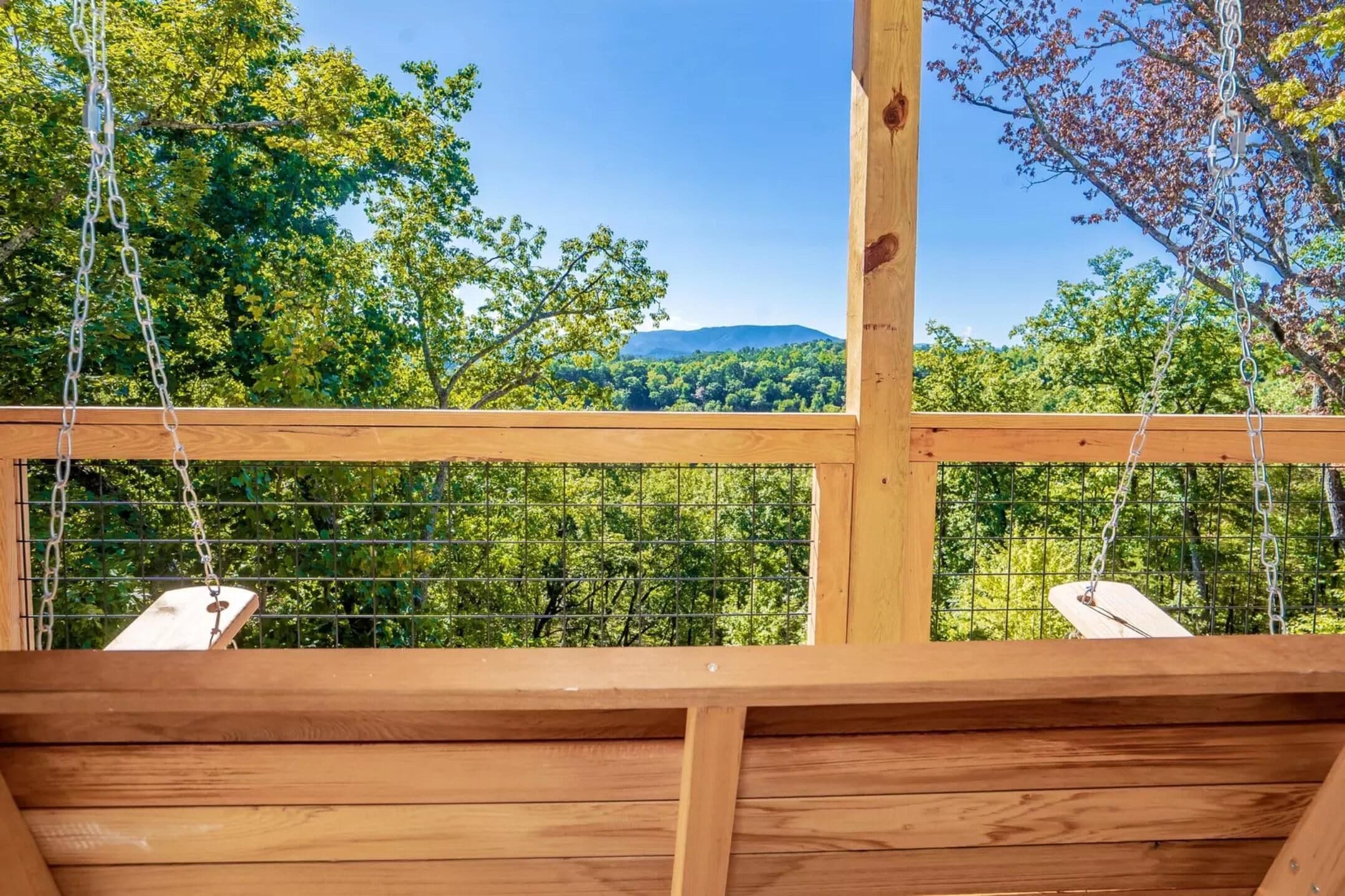 A wooden deck with a metal railing, offering a view of a forested landscape with trees and a distant hill.