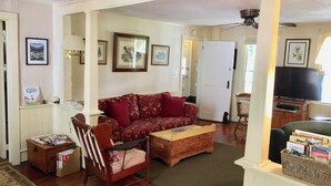 Una sala de estar con un sofá rojo estampado, una mesa de centro de madera, una silla de madera, un televisor y cuadros en la pared.