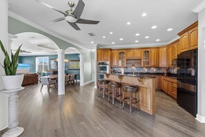 Une cuisine moderne avec des meubles en bois, un îlot central doté de tabourets et un ventilateur de plafond.