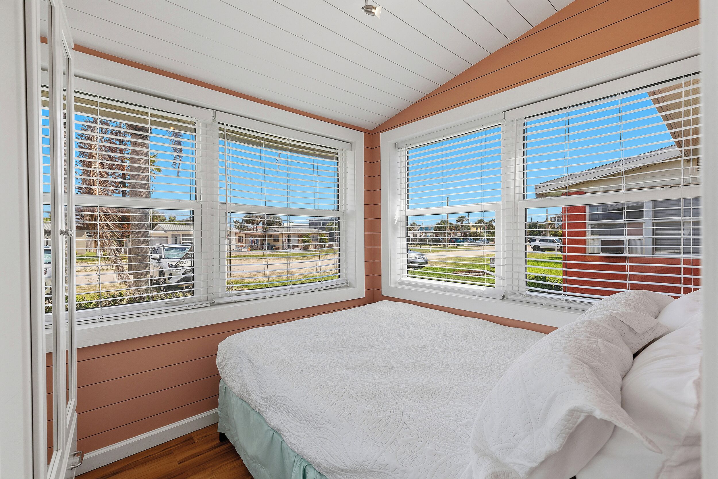 Un dormitorio con cama, persianas blancas y vistas al exterior.