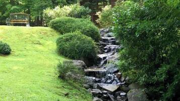 A garden with a small waterfall, neatly trimmed bushes, and a wooden bench.