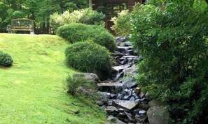 Um jardim com uma pequena cascata, arbustos bem aparados e um banco de madeira.