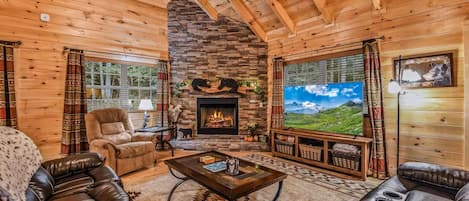 A log cabin interior with a fireplace, leather sofas, a television, and a stone wall.