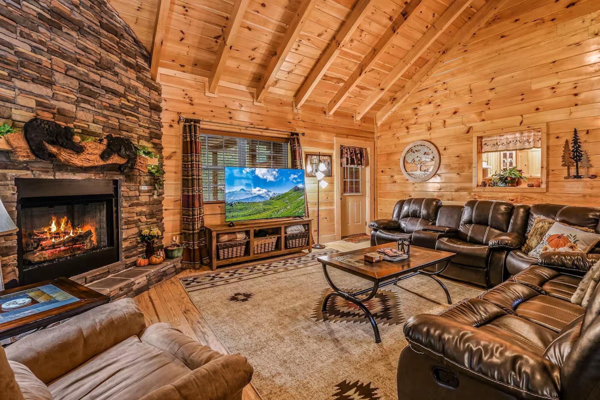 A cozy log cabin interior with a fireplace, leather furniture, and a large TV screen.