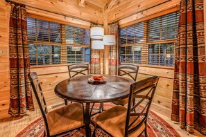 A wooden interior with a round table, four chairs, patterned curtains, and a window with blinds. - Bamboo Hideaway (Gatlinburg)