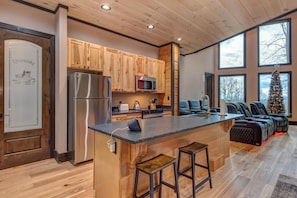 A kitchen with wooden cabinets, a stainless steel refrigerator, a microwave, and a bar area with stools. - Waterfalls and Wildflowers (Gatlinburg)