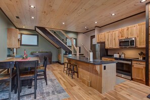 A modern kitchen with wooden cabinetry, a central island, bar stools, and a staircase leading to another level. - Waterfalls and Wildflowers (Gatlinburg)