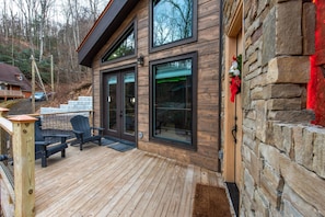 A wooden deck with outdoor seating, a stone wall, and a glass door entrance. - Waterfalls and Wildflowers (Gatlinburg)