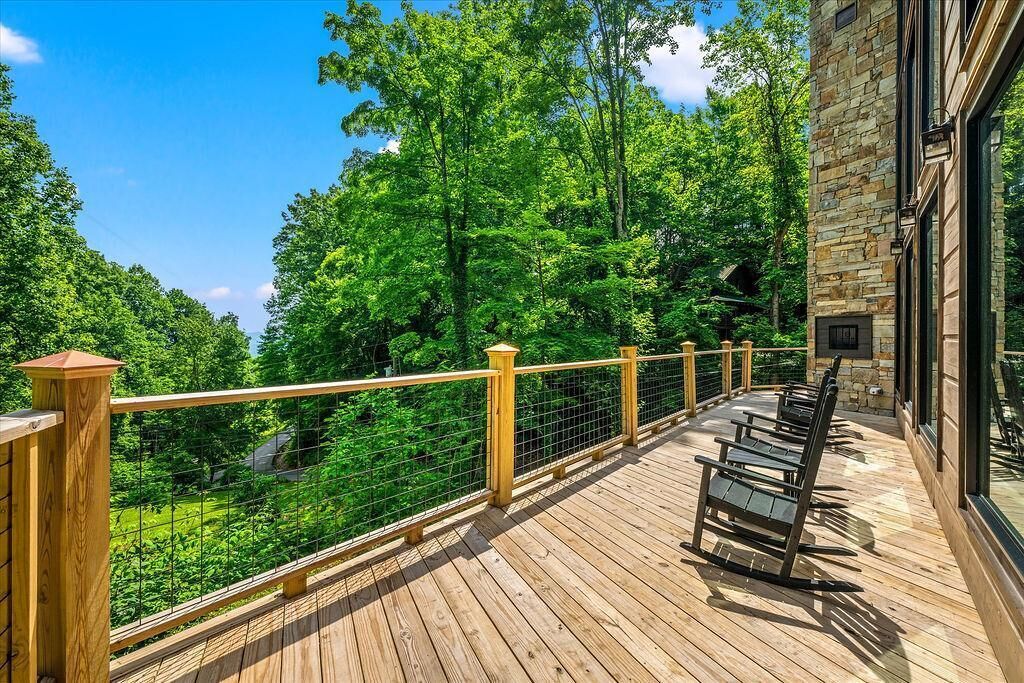 A wooden deck with a stone building, a metal railing, and a view of a forest.