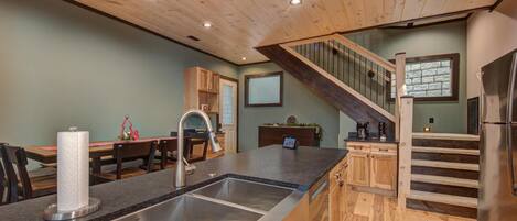 A kitchen with a stainless steel sink, wooden cabinets, a dining area with a table and chairs, and a staircase leading to an upper level.
