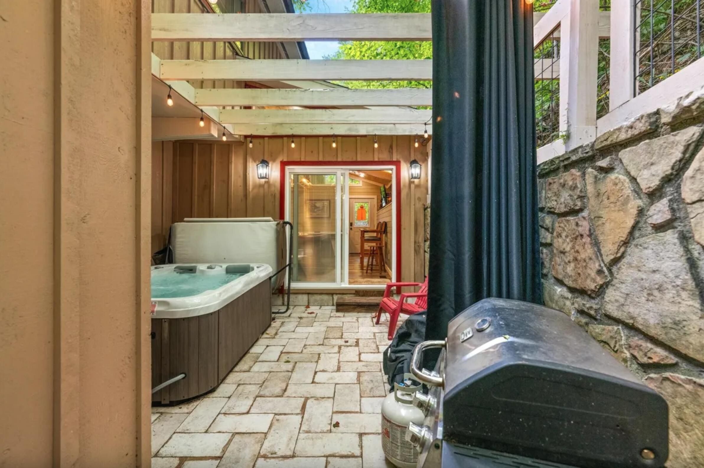A hot tub, outdoor seating, and a grill area in a covered patio.
