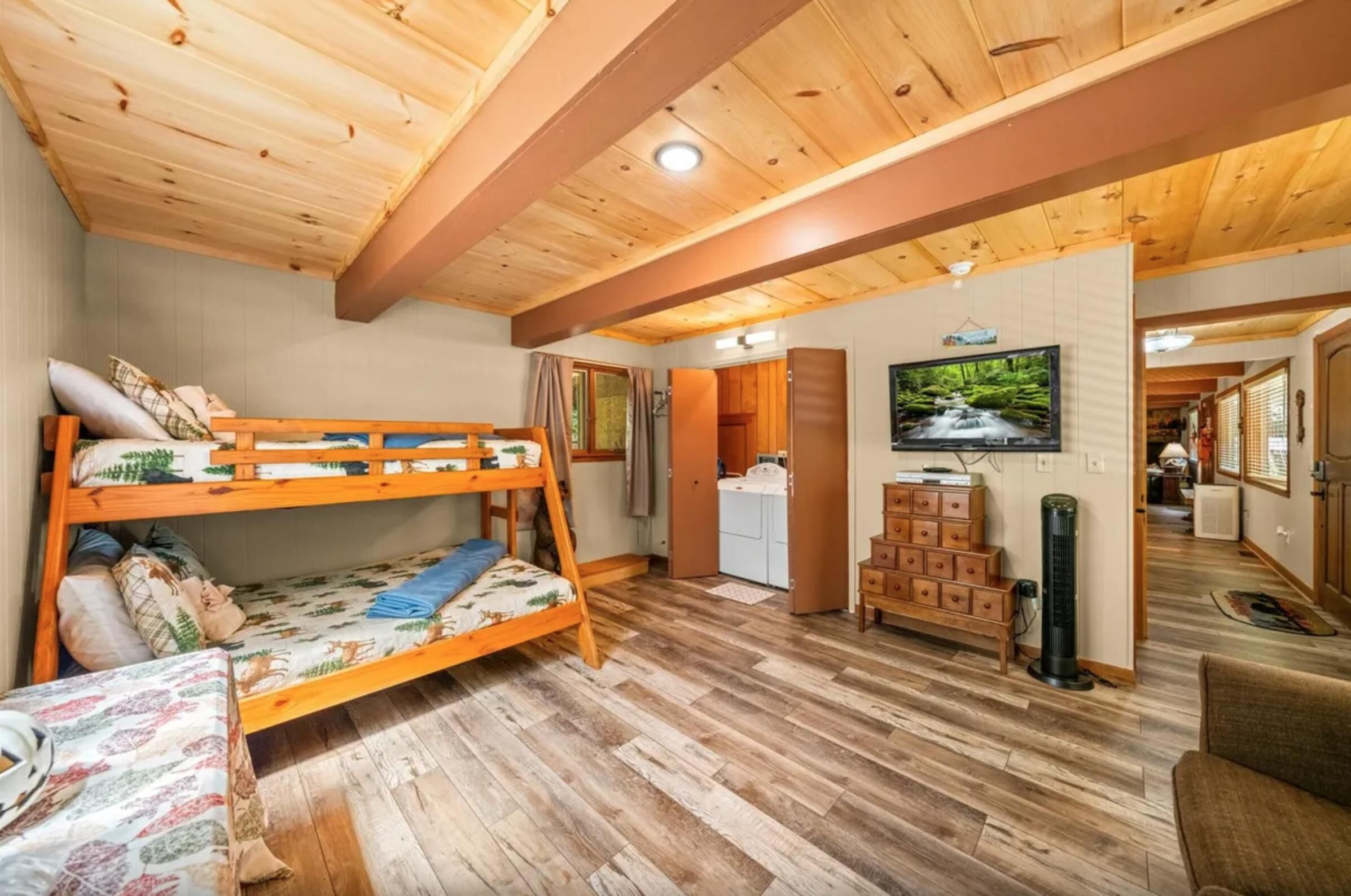A room with a bunk bed, a small table, a TV, and a kitchenette.