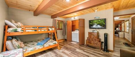 A room with a bunk bed, a small table, a TV, and a kitchenette.