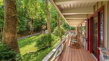 A wooden deck with a railing, surrounded by trees and greenery.