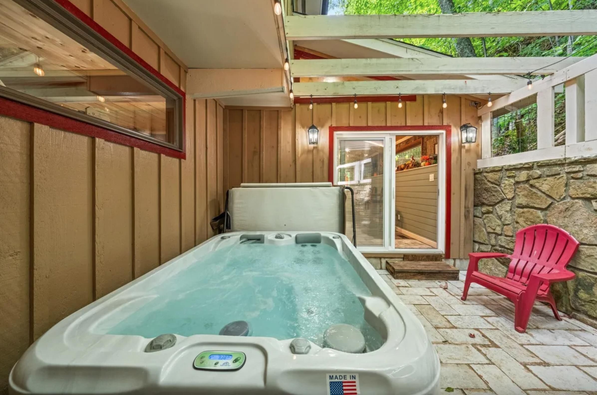 Un bain à remous doté d’un panneau de commande, une chaise Adirondack rouge et un mur en pierre.