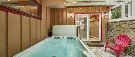 Un bain à remous doté d’un panneau de commande, une chaise Adirondack rouge et un mur en pierre.