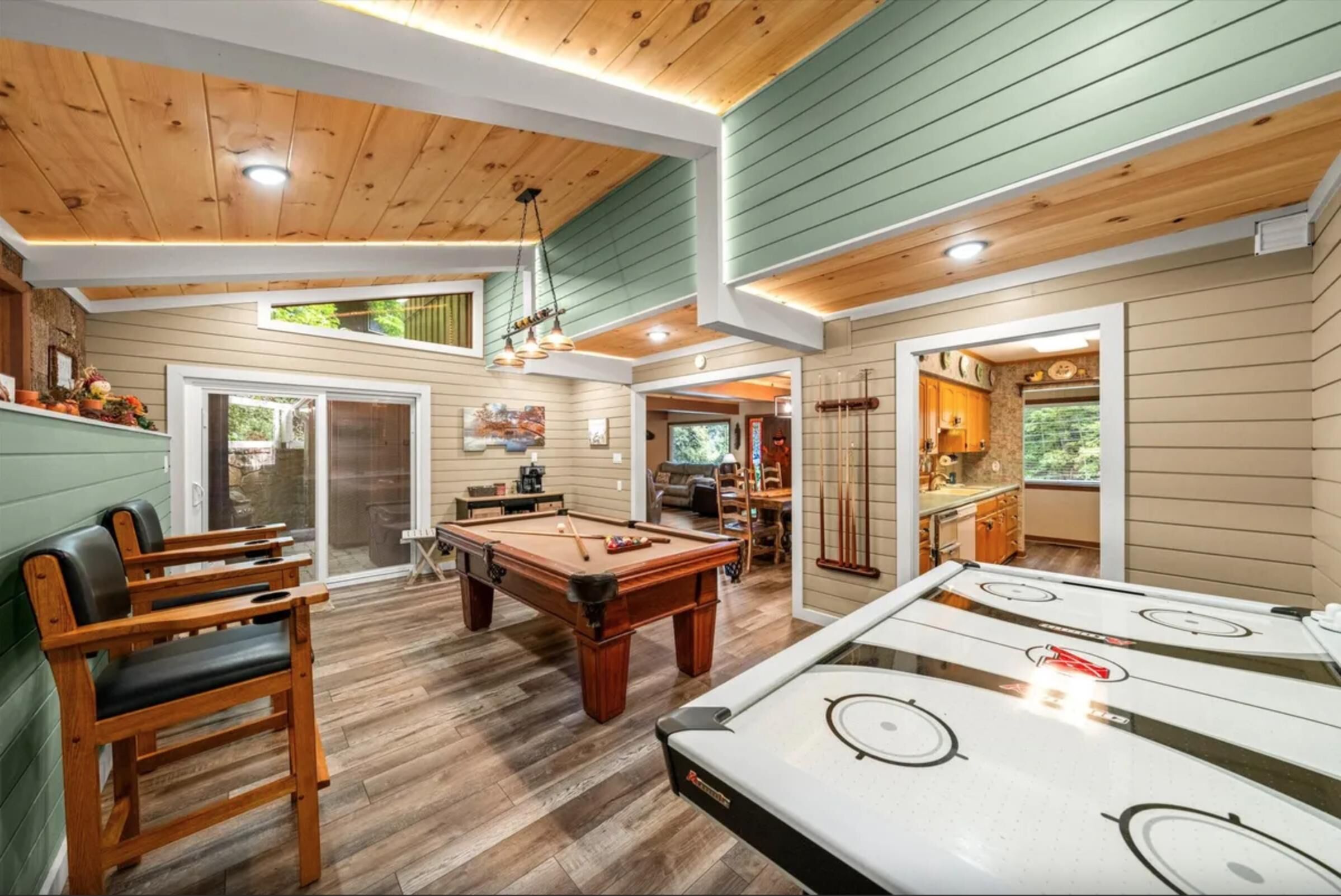 A pool table, a billiards table, and a pool cue rack in a room with wooden floors and walls.