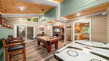 A pool table, a billiards table, and a pool cue rack in a room with wooden floors and walls.