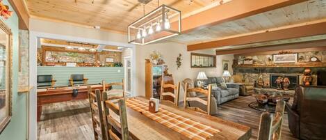 A rustic interior with a wooden dining table, chairs, a fireplace, and a cozy seating area.