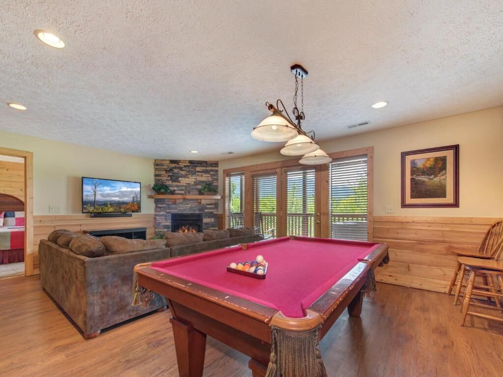 A pool table in a room with a stone fireplace, wooden benches, and a television.