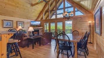 A spacious wooden interior with a high ceiling, a fireplace, a dining area, and large windows.