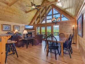 A spacious wooden interior with a high ceiling, a fireplace, a dining area, and large windows. - Eagles Point Lodge (Gatlinburg)