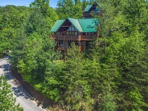 A cabin surrounded by dense forest, with a prominent green roof and multiple decks. - Eagles Point Lodge (Gatlinburg)