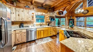 A wooden cabin interior with a kitchen featuring granite countertops, wooden cabinets, a stainless steel refrigerator, and a built-in stove. - Bear Tracks (Sevierville)