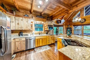 A wooden cabin interior with a kitchen featuring granite countertops, wooden cabinets, a stainless steel refrigerator, and a built-in stove. - Bear Tracks (Sevierville)