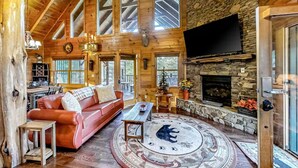 A log cabin interior with a stone fireplace, leather sofa, and a large TV mounted on the wall. - Bear Tracks (Sevierville)