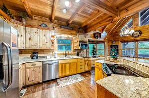 A wooden cabin interior with a kitchen featuring granite countertops, wooden cabinets, a stainless steel refrigerator, and a built-in stove. - Bear Tracks (Sevierville)