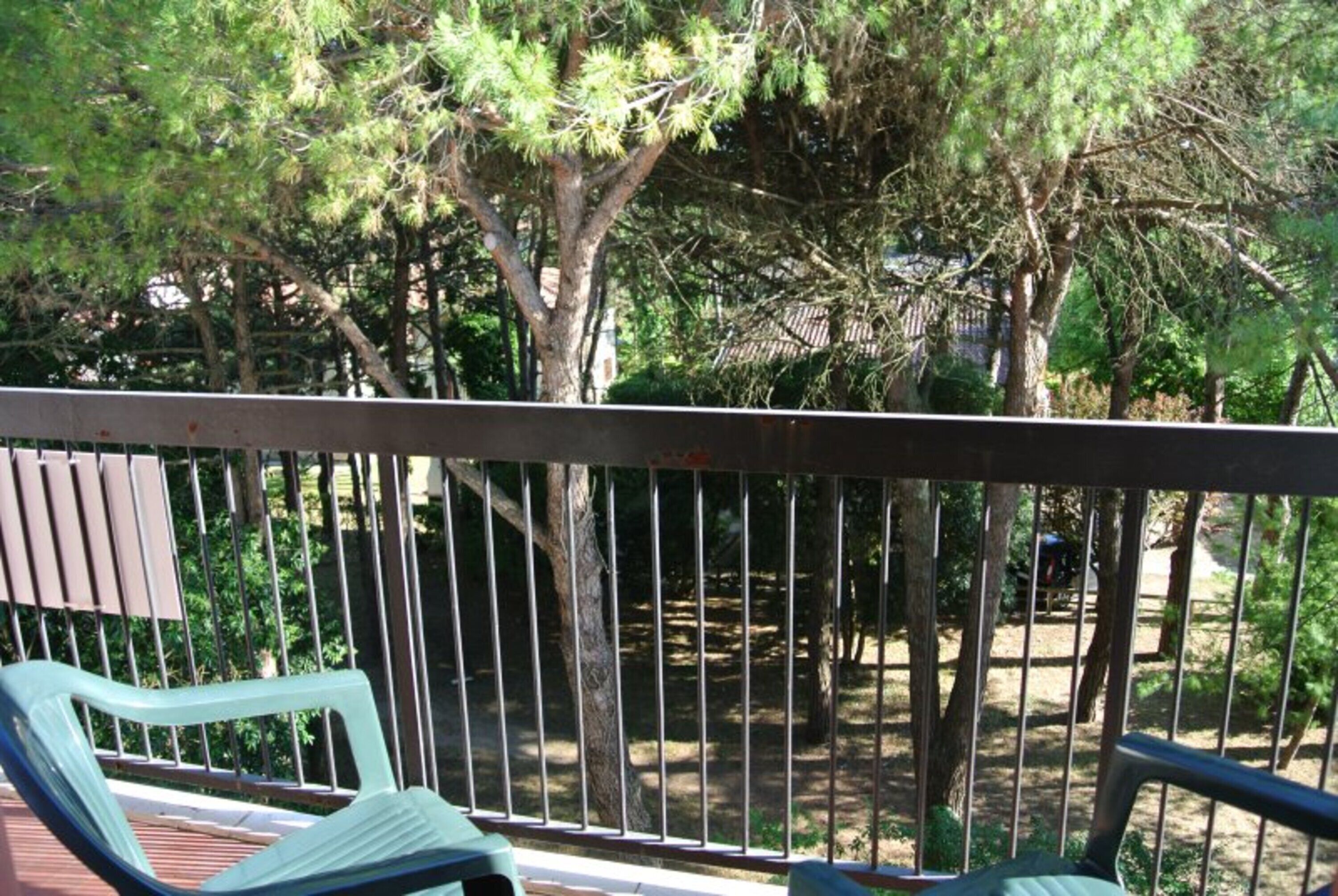 Ein Balkon mit Metallgeländer, einer Holzterrasse und Blick auf Bäume und einen Garten.