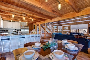A spacious kitchen with wooden beams, a dining area with a table set for four, and a living area with a sofa and a staircase. - Mountain Grace Lake Retreat (Sevierville)