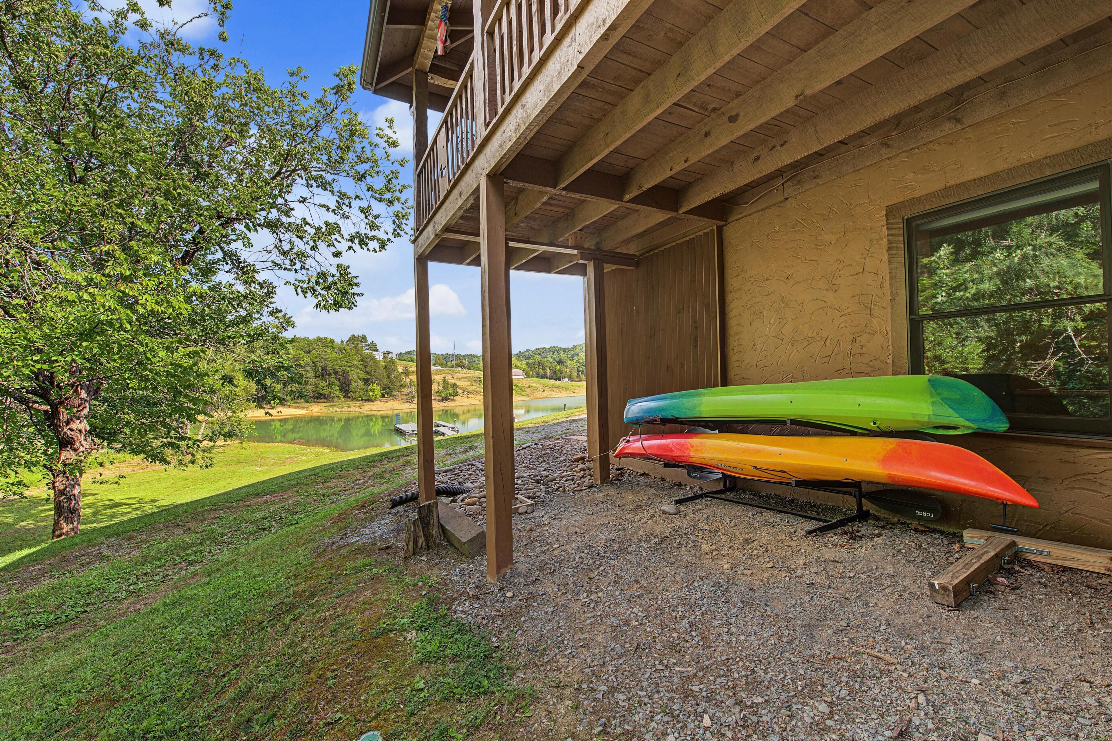 A covered outdoor area with a view of a lake, wooden deck, and kayaks.