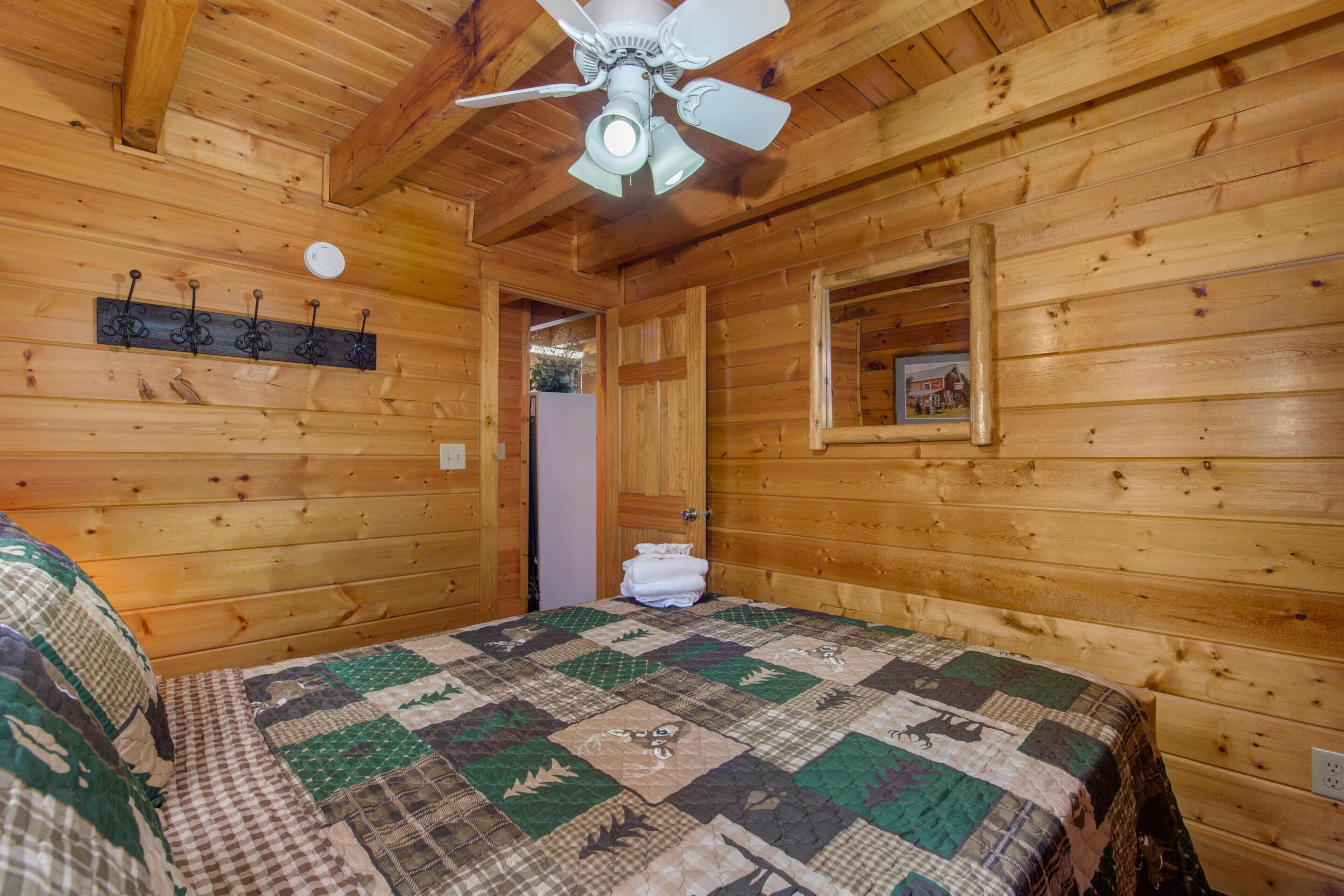 Ein Schlafzimmer einer Holzhütte mit gesteppter Bettdecke, Deckenventilator und kleinem Fenster.