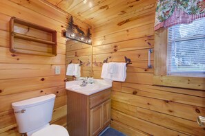 A wooden cabin bathroom with a toilet, sink, and mirror. - Bearcation (Pigeon Forge)
