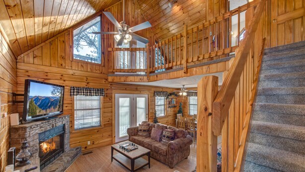 L’intérieur d’une cabane en rondins, avec une cheminée, un canapé, un coin repas et un escalier.