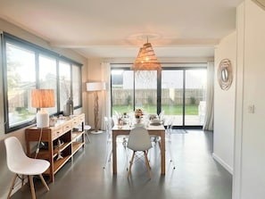 Ein Essbereich mit einem Tisch für vier Personen, einer modernen Lampe und Blick auf den Garten durch große Fenster.